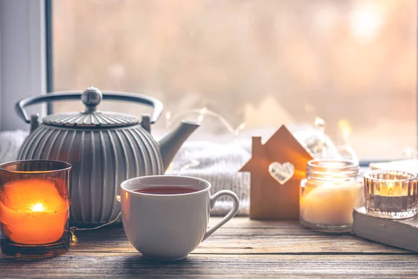 Bir fincan çay, mumlar ve çaydanlıkla rahat bir ev kompozisyonu. Pencere kenarındaki ev rahatlığı. Boşluğu kopyala.