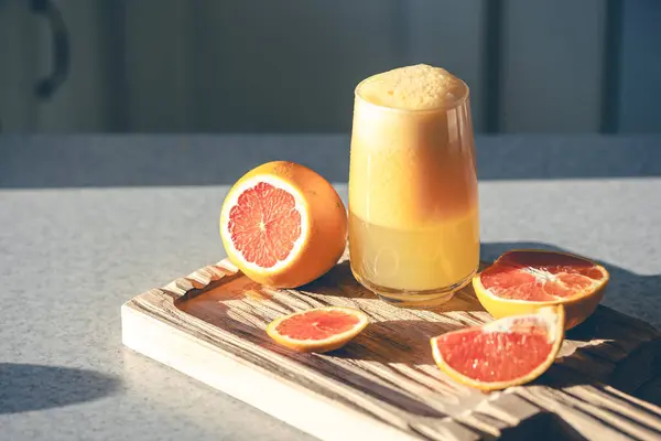 A glass of freshly squeezed juice and orange fruit on a wooden cutting board on the kitchen table. Squeezed fruit juice at home, copy space.