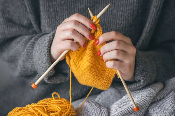 Kırmızı tırnaklı bir kadının elleri sarı iplikten örülür. El yapımı giysiler. Kız hobileri için içeri giriyor..