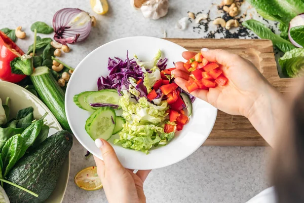 Mutfaktaki bayanların elinde taze sebze dilimlenmiş bir tabak, üst manzara. Bir kadın evde sağlıklı bir salata hazırlar. Sağlıklı yeme kavramı.