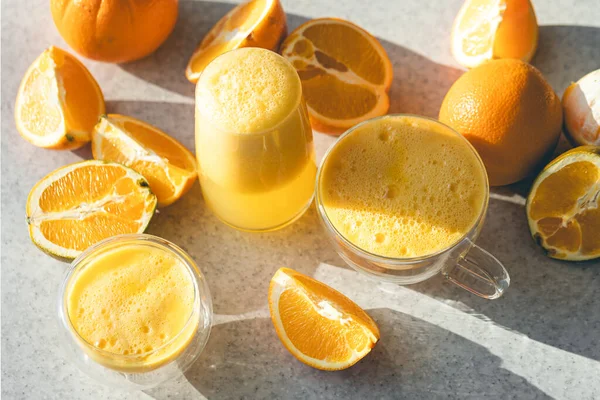 Glasses of freshly squeezed orange juice and fruit oranges on the kitchen table. Preparing fresh orange juice. Making natural juice at home.