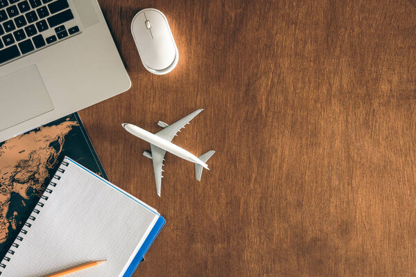 Travel concept, airplane miniature, notepad, World map and laptop on a wooden table. Copy space.