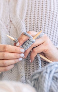Dairesel iğneler kullanarak örgü ören ellerin yakın çekimi. Kadın kalın iplikten örgü örüyor. El yapımı giysiler. Kız hobileri için içeri giriyor..