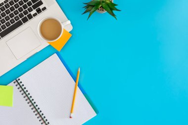Ofis iş yeri konsepti. Mavi arka planda dizüstü bilgisayar ve bir fincan kahve. Kopyalama alanı olan üst görünüm, düz yatay.