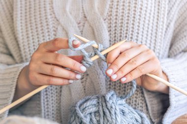 Dairesel iğneler kullanarak örgü ören ellerin yakın çekimi. Kadın kalın iplikten örgü örüyor. El yapımı giysiler. Kız hobileri için içeri giriyor..