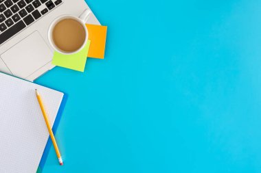 Ofis iş yeri konsepti. Mavi arka planda dizüstü bilgisayar ve bir fincan kahve. Kopyalama alanı olan üst görünüm, düz yatay.