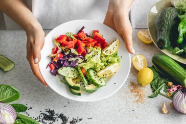 Mutfaktaki bayanların ellerinde taze sebze dilimlenmiş bir tabak. Biber salatası, lahana ve salatalık. Çiğ sebze salatası, vejetaryen..