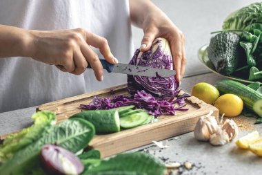 Bir kadın kesme tahtasıyla sebze kesiyor. Bir kadın ahşap bir tahtada lahana ve salatalık kesiyor, yakın plan..