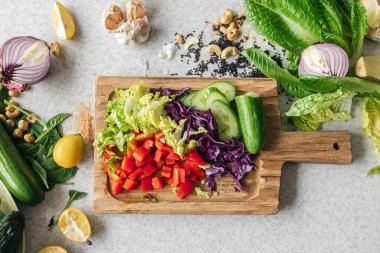 Ahşap mutfak tahtasında dilimlenmiş lahana, dolmalık biber ve salatalık. Evde taze sebzelerle salata pişirmek. Üst görünüm.
