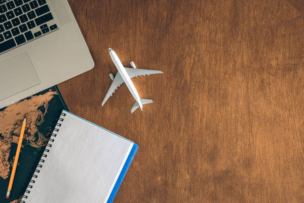 Travel concept, airplane miniature, notepad, World map and laptop on a wooden table. Copy space.