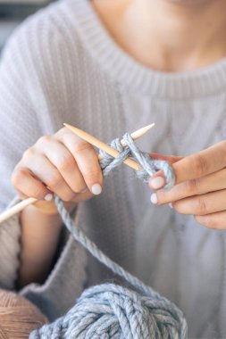 Dairesel iğneler kullanarak örgü ören ellerin yakın çekimi. Kadın kalın iplikten örgü örüyor. El yapımı giysiler. Kız hobileri için içeri giriyor..