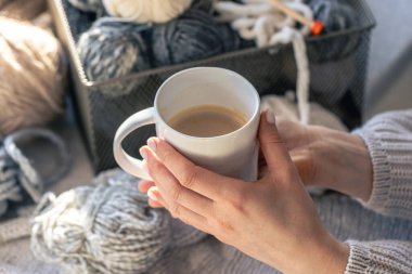 Kadın ellerinde bir fincan kahve ve iplik ipliği. Ev konforu, hobi olarak örgü örmek..