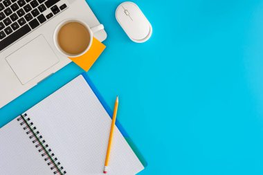 Ofis iş yeri konsepti. Mavi arka planda dizüstü bilgisayar ve bir fincan kahve. Kopyalama alanı olan üst görünüm, düz yatay.