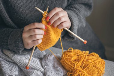 Kırmızı tırnaklı bir kadının elleri sarı iplikten örülür. El yapımı giysiler. Kız hobileri için içeri giriyor..