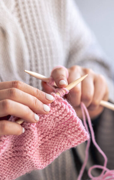 Крупный план женских рук, вяжущих розовый шерстяной свитер. Девушка занимается своими хобби. Концепция вязания.