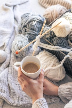 Kadın ellerinde bir fincan kahve ve iplik ipliği. Ev konforu, hobi olarak örgü örmek..