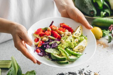 Mutfaktaki bayanların ellerinde taze sebze dilimlenmiş bir tabak. Biber salatası, lahana ve salatalık. Çiğ sebze salatası, vejetaryen..