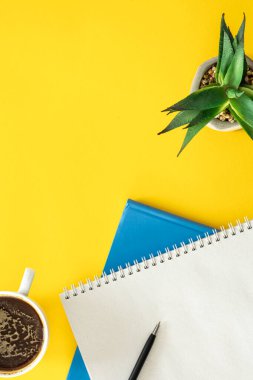 Not defterleri ve sarı arka planda bir fincan kahve. Asgari arkaplan, kopyalama alanı.