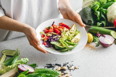 Mutfaktaki bayanların ellerinde taze sebze dilimlenmiş bir tabak. Sağlıklı yeme kavramı.