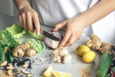 Bir kadın mutfak masasında salata için soğan doğruyor, yakın plan. Kadın elinde yarım soğan, sağlıklı bir yemek hazırlıyor..