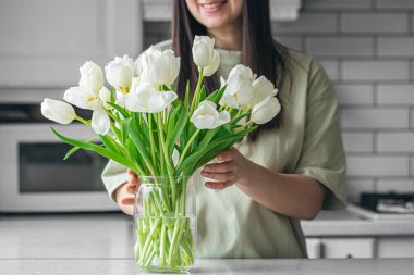 Mutfaktaki vazoya bir buket beyaz lale çiçeği koyan kadın. Uluslararası Kadın Günü konsepti.