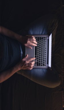 Gece geç saatlerde dizüstü bilgisayar başında meşgul bir adam, mesaj yazıyor, fazla mesai yapıyor, internette sörf yapıyor. Aşırı çalışma ve uzaktan çalışma konsepti. Karanlık odada sergilenen ışıktan.