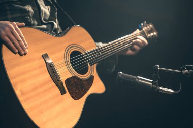 Erkek müzisyen kayıt stüdyosunda mikrofonun arkasında akustik gitar çalıyor. Müzik kaydı, prova ya da canlı performans kavramı.