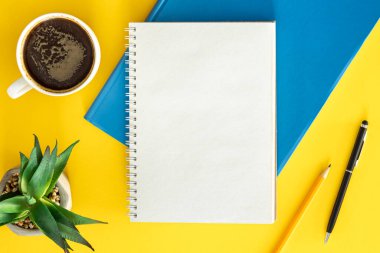 Ofis arkaplan tasarımı, boş not defteriyle düz uzanma, sarı arka planda bir fincan kahve ve bitki, üst manzara..