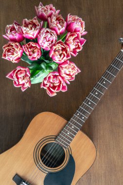 Ahşap arka planda pembe laleler ve akustik gitarlar, üst manzara. Bahar çiçekleri ve gitar masada..