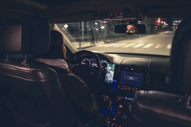 Şehirde geceleri modern arabasını kullanan genç bir kadın navigatör kullanıyor. Gece yolu, arabanın içi manzaralı..