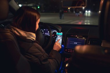 Şehirde geceleri modern arabasını kullanan genç bir kadın navigatör kullanıyor. Gece yolu, arabanın içi manzaralı..