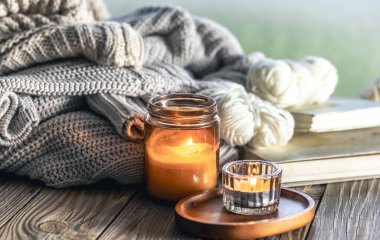 Yanan mumlarla ev kompozisyonu, ahşap bir yüzey üzerinde örülmüş elementler ve kitaplar..