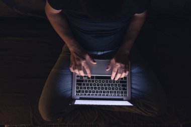 Gece geç saatlerde dizüstü bilgisayar başında meşgul bir adam, mesaj yazıyor, fazla mesai yapıyor, internette sörf yapıyor. Aşırı çalışma ve uzaktan çalışma konsepti. Karanlık odada sergilenen ışıktan.