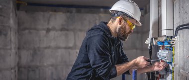 Erkek bir elektrikçi elektrik kablosuyla santralde çalışıyor. Boşluğu kopyala.