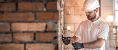 Elinde bir aletle inşaat alanında kabloyla çalışan bir elektrik kurucusu. Tamir ve tamirci konsepti. Ev ve ev yeniden yapılandırması.