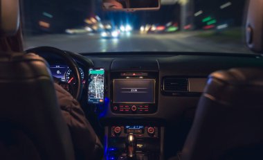 Şehirde geceleri modern arabasını kullanan genç bir kadın navigatör kullanıyor. Gece yolu, arabanın içi manzaralı..