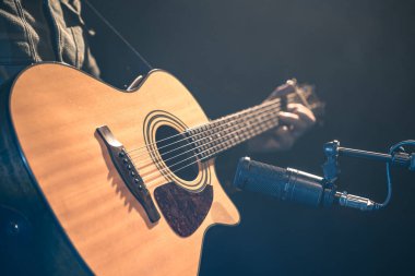 Erkek müzisyen kayıt stüdyosunda mikrofonun arkasında akustik gitar çalıyor. Müzik kaydı, prova ya da canlı performans kavramı.