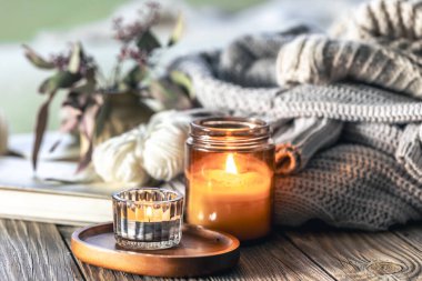 Yanan mumlarla ev kompozisyonu, ahşap bir yüzey üzerinde örülmüş elementler ve kitaplar..