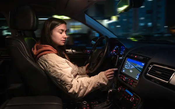 Attractive young woman driving a car at night. Driving a car at night, a woman driving her modern car at night in the city.