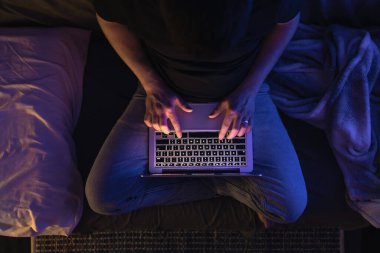 Gece geç saatlerde dizüstü bilgisayar başında meşgul bir adam, mesaj yazıyor, fazla mesai yapıyor, internette sörf yapıyor. Aşırı çalışma ve uzaktan çalışma konsepti. Karanlık odada sergilenen ışıktan.
