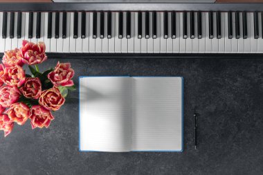 Piyano, bir buket lale çiçeği ve arka planda bir not defteri, üst manzara. Müzik öğrenme kavramı, kopyalama alanı.