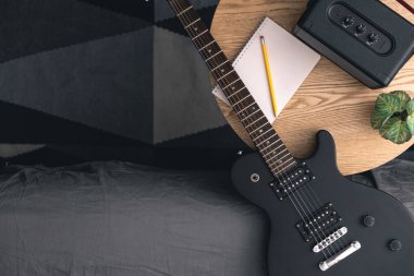 Siyah bir elektro gitar, kalem ve müzik hoparlörü olan bir not defteri. Gitar çalmayı öğrenme, şarkı yazma kavramı. Boşluğu kopyala.