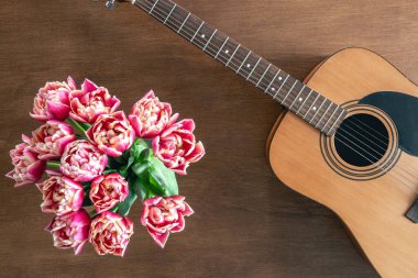 Ahşap arka planda pembe laleler ve akustik gitarlar, üst manzara. Bahar çiçekleri ve gitar masada..