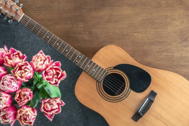 Ahşap arka planda pembe laleler ve akustik gitarlar, üst manzara. Bahar çiçekleri ve gitar masada..