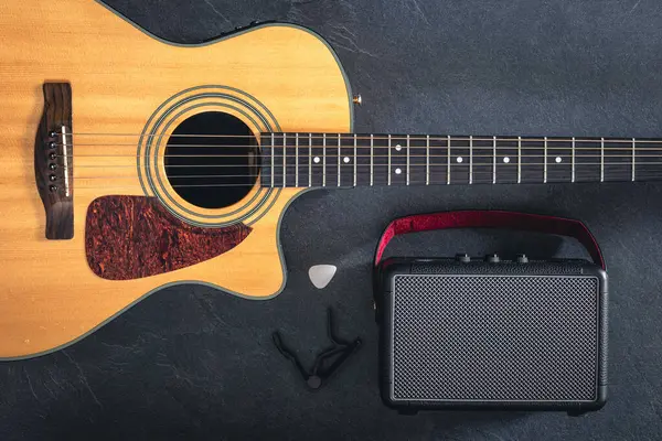 Acoustic guitar and speaker on a black background, top view. Musical background, concept of rehearsal, learning to play the guitar.