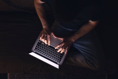 Gece geç saatlerde dizüstü bilgisayar başında meşgul bir adam, mesaj yazıyor, fazla mesai yapıyor, internette sörf yapıyor. Aşırı çalışma ve uzaktan çalışma konsepti. Karanlık odada sergilenen ışıktan.
