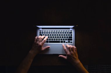Adam yazarak kullanma dizüstü bilgisayar karanlık geceleri çalışıyor. Üstten Görünüm işyeri yazar düz yatıyordu.