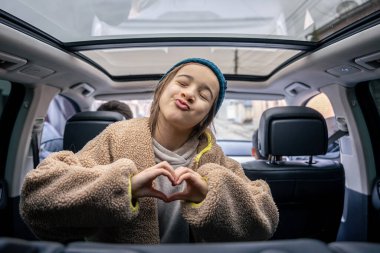 Arabanın arka koltuğunda poz veren, arabada oynayan komik küçük kız. Yolculuk kavramı. Otomobille seyahat ederken, ebeveynler ve kızları yolculuğun tadını çıkarıyorlar..