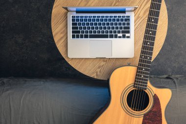 Tahta bir masada akustik gitar ve dizüstü bilgisayar, üst manzara. Müzik ve teknoloji, dijital konsept. Online gitar dersleri.
