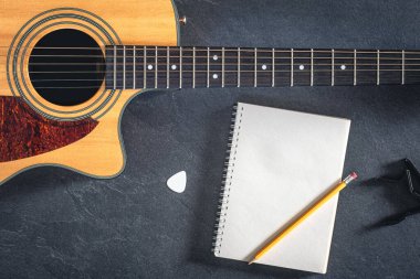 Siyah desenli arka planda akustik gitar ve defter, üst görünüm. Gitarla yakın plan müzik arkaplanı.